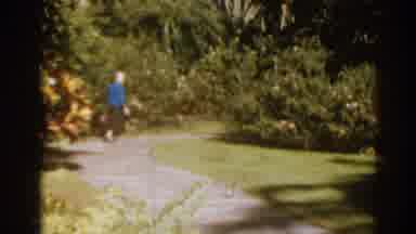Florida USA (1963): Woman Wearing Blue Sweater Looks At Red Blooming Flowers On A