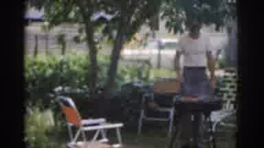 New Jersey USA (1963): Man Grilling In Yard Next To A Tree Child Walks Past Picnic