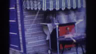 New Jersey USA (1963): Woman Wearing Striped Shirt Checks Food Cooking On Outdoor
