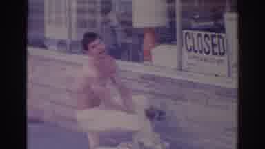 Temple City California (1966): A Shirtless Young Man Squats In Front Of A Shop And