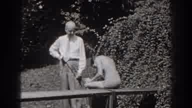 New Jersey (1938): Man Wearing White Shirt Stands Next To Woman Sitting On Bench