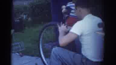 York Nebraska (1958): A Man Sits And Works On A Bicycle Tire While A Boy Stands
