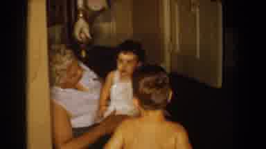 Bel Air Maryland (1960): Baby Wearing White Overalls Stands In Between Brown Sofa