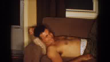 Bel Air Maryland (1960): Man Wearing Grey Pants Relaxes On Tan Sofa While Woman
