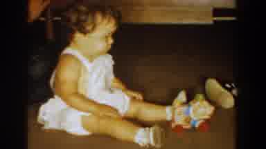 Bel Air Maryland (1960): Baby Wearing White Romper Sits On Floor Watching Toy Roll