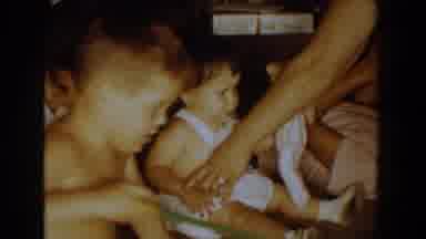 Bel Air Maryland (1960): Adult Arms Pull Baby Girls Arm Forward To Grasp A Doll