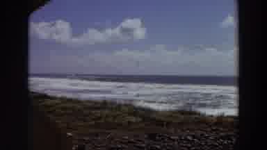 California (1964): Waves Come Ashore On A Rocky Beach Dotted With Vegetation On A