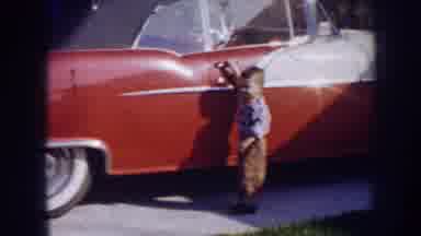 Nebraska (1956): Boy Wearing Blue Shirt Stands Next To Redbrick And White Car On A