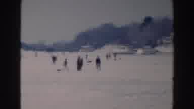 Tustin Wisconsin (1964): People Walk Across A Frozen Lake While Trees And Homes