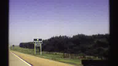 Nebraska (1969): Moving Landscape With Trees And Mountains And A Sign That Reads