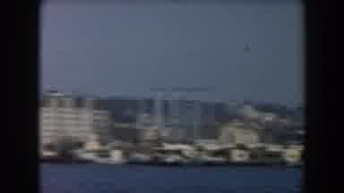 California (1961): View Of White City Buildings Blue Ocean Water And Grey Ship On