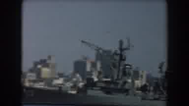 California (1961): View Of Grey Ship And White City Buildings Along Sea Port On A