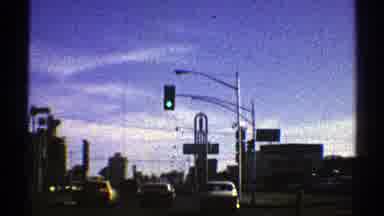 Nevada (1969): Cars Driving Along A Street With Traffic Lights In A City With Tall