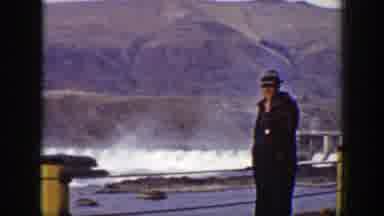 California (1938): Man Wearing Grey Hat Watches Dam Release Water On A Clear Day
