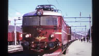 Norway (1976): Large Red Train Sits On Tracks In Train Yard While People Walk