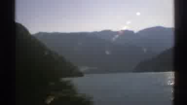 Norway (1976): A Vehicle Passes By A Mountain Lake Surrounded By A Forest Of