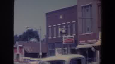 Iowa (1959): Cars Are Parked On A Street In Front Of Window Shops With Two Stories