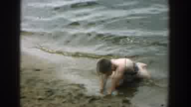 Wisconsin (1957): Boy Wearing Blue Shorts Kneels In Sand On A Clear Day