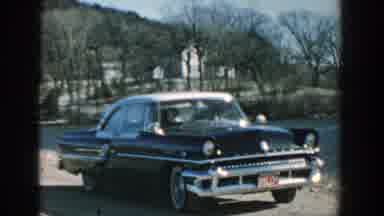 Wisconsin (1957): Some People Inside A Black Car And A Landscape With Trees In The