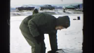 Wisconsin (1957): Man Wearing Grey Coat Holds Small Grey Fish On A Clear Day