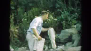 Connecticut (1947): Man Wearing Blue Shirt Picks Up White Object On A Bright Sunny