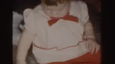 Nebraska (1955): Chubby Baby Wearing A White And Red Dress Plays With Rice