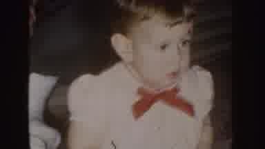 Nebraska (1955): A Baby With A Red Bow Around His Neck Sitting On The Floor