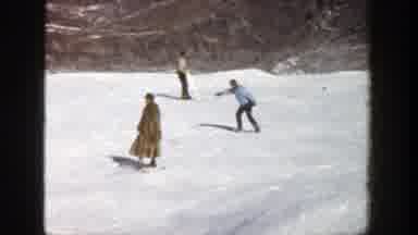 Aspen Colorado (1961): Person Wearing Brown Fur Coat Skis Backwards On A Sunny Day