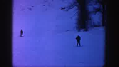 Aspen Colorado (1961): Two People Skiing Downhill Past Trees On A Clear Winter Day