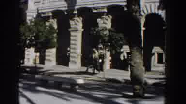 Italy (1960): Black Car Drives By Beige Stone Building On A Sunny Day