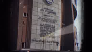 Baltimore Maryland (1961): A Vehicle Drives By A Large Building And Is Passed By A
