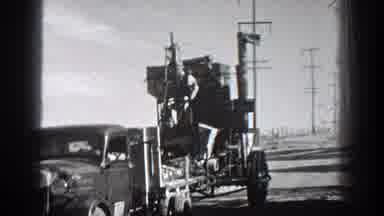 California-1936: A Truck Driver Waves While His Truck Pulls Farm Machinery On A