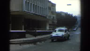 Israel (1960): Vintage Car Moves In Front Of A Tall Building With Passersby