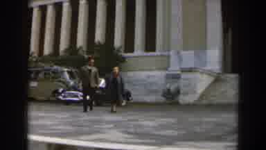 Israel (1960): Man And Woman Wearing Grey Coats Walk Away From Yellow Building