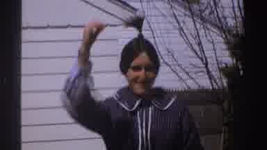 Michigan (1969): Woman Wearing Blue Shirt Stands Near White Building On A Bright
