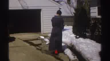 Michigan (1969): Person Wearing Grey Robe Stands Near Open Garage Of A White House