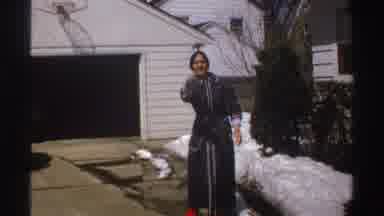 Michigan (1969): A Woman Wearing A Robe Stands In A Driveway In Front Of A Garage