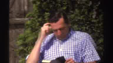 Michigan (1969): Man Sitting In The Yard Reading With Fence And Greenery In The