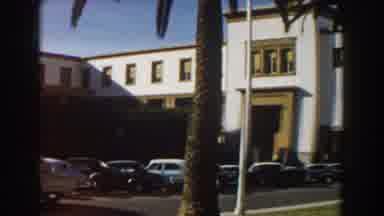CASABLANCA-1959: Cars Drive By A Long White Building With A Parking Lot And Palm Trees