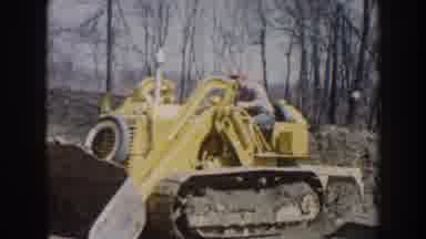 Nebraska (1959): Man Wearing Blue Pants Drives Yellow Bulldozer On A Clear Day