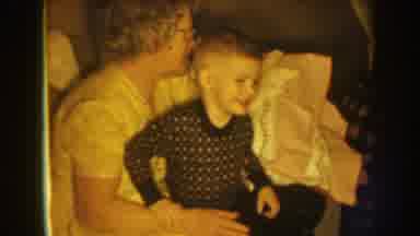 Nebraska (1959): Woman Wearing White Dress Holds Small Boy Wearing Black Pajamas