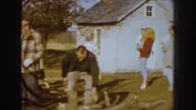 Nebraska (1959): Several Women In Front Of A House And Two Men Carrying Wood On A