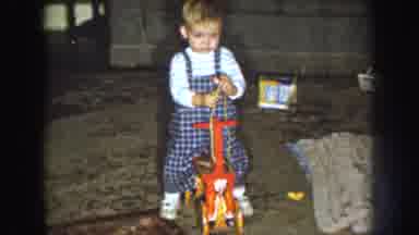 Nebraska (1959): Toddler Wearing Blue Overalls Holds Yellow String While Sitting