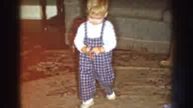 Nebraska (1959): A Young Child Walks On The Carpet Inside Of A House While A Car