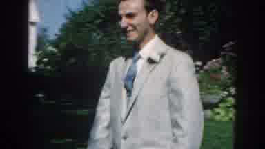 Nebraska (1959): Man Wearing Grey Suit Walks Past A White House On A Sunny Day