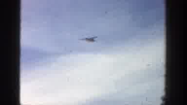 Aspen Colorado (1961): View Of White Plane Flying Under Clouds On A Clear Day