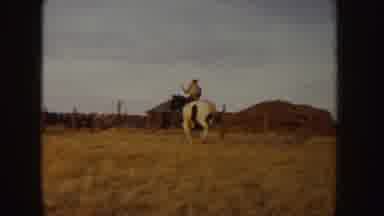 Idaho (1955): Two People Ride Horses Across A Field Toward A Red Car Parked Near