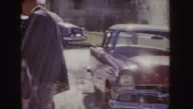 Idaho (1955): Older Vehicles Parked And A Red Vehicle With White Stripe Driving
