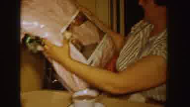 Idaho (1955): Woman Wearing White Shirt Looks At Plastic Wrapped Item At Table