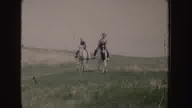 Idaho (1955): Two People Riding Horses Through Green Field On A Sunny Day